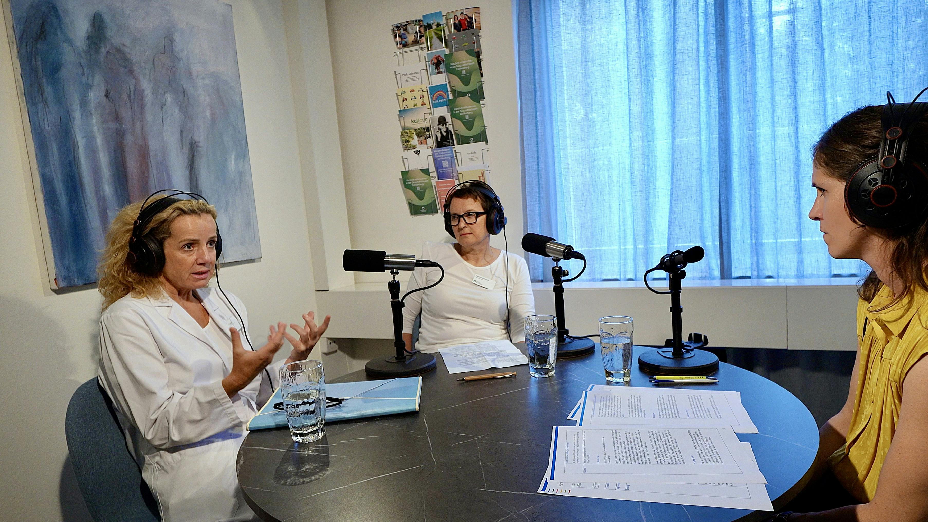 Zwei Personen bei einer Podcast-Aufnahme mit Mikrofonen und Unterlagen auf einem Tisch.