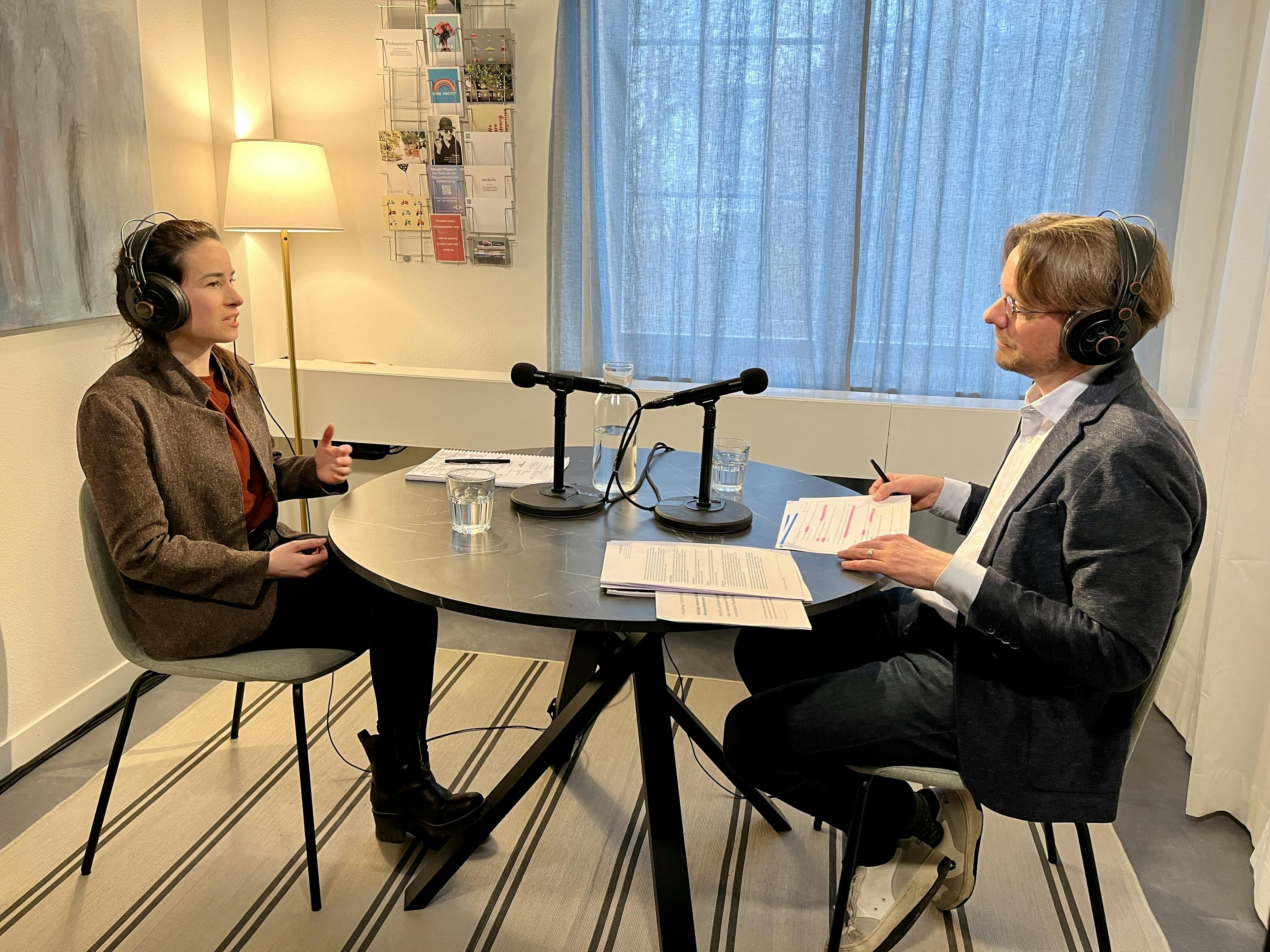 Zwei Personen bei einem Podcast-Interview in einem Studio mit Mikrofonen und Kopfhörern.