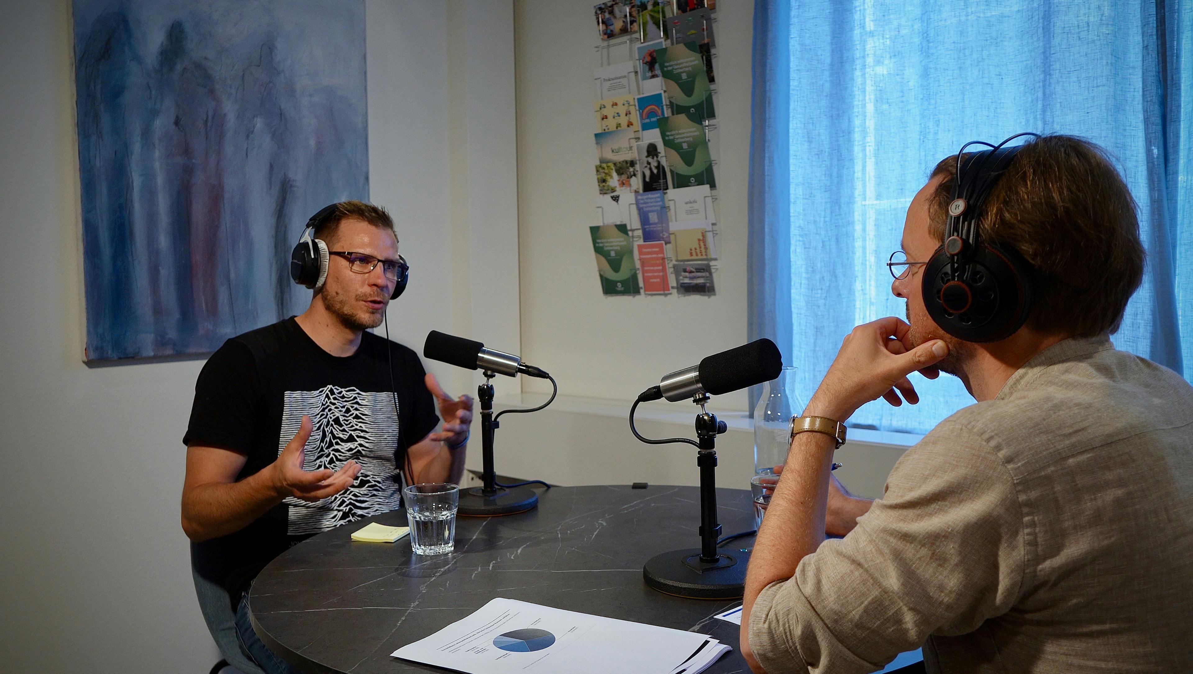 Zwei Männer beim Podcast-Interview in einem Studio mit Mikrofonen und Kopfhörern.