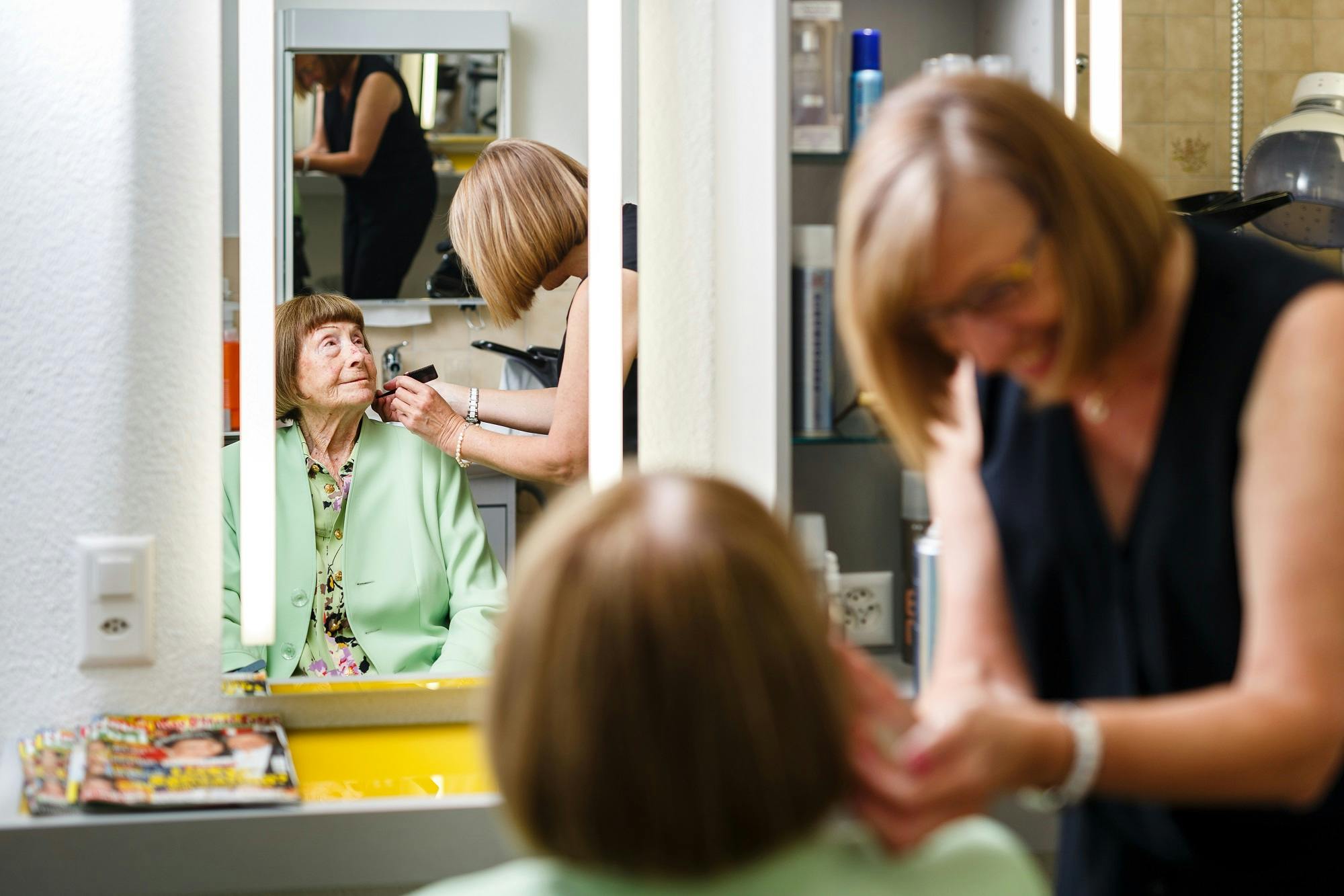 Eine ältere Dame wird in einem Friseursalon von einer Friseurin gestylt, Spiegelbild im Vordergrund.