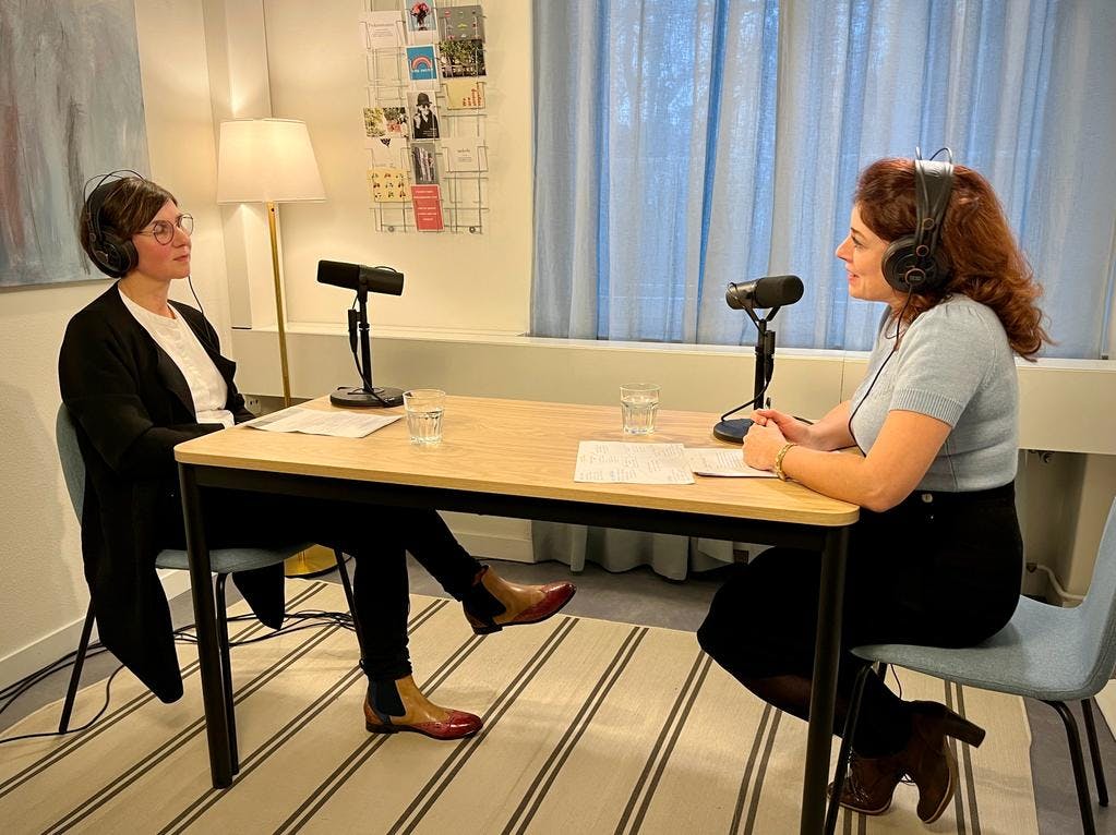Zwei Personen bei einem Podcast-Interview in einem Innenraum.