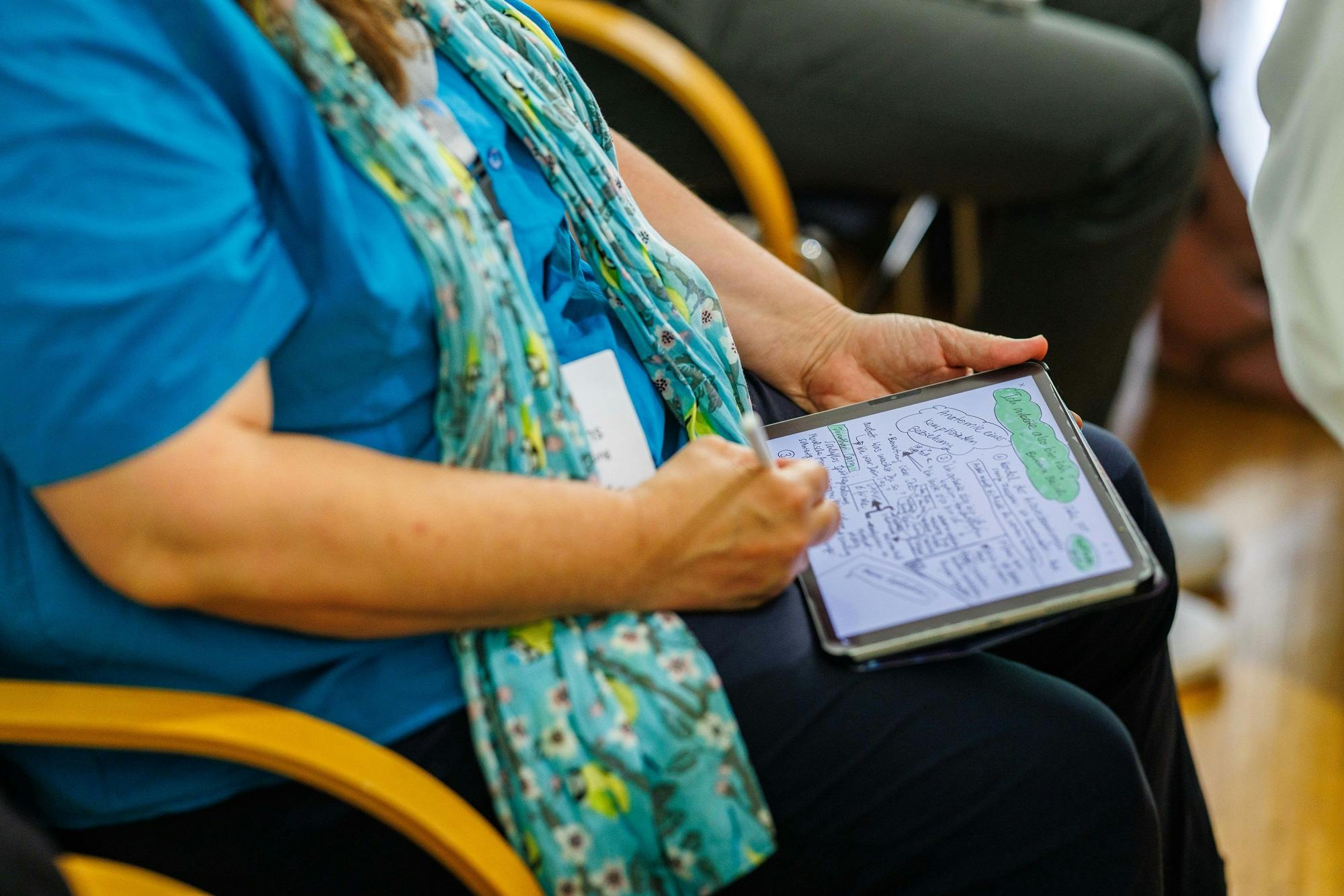 Person macht sich Notizen auf einem Tablet bei einer Konferenz oder einem Workshop.